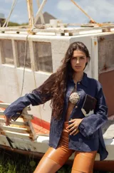 Camisa color naranja de lino o algodón con cuello clásico, cierre frontal con botones y mangas largas con puños abotonados. Presenta un bolsillo de cuero marrón en el pecho.