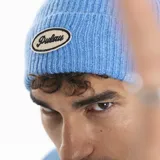 Gorro tipo beanie tejido en punto acanalado, con parche ovalado bordado en la parte frontal que incluye el logo de la marca.