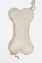 Monedero pequeño de cuero reconstituido color rojo brillante, con forma de hueso de perro. Posee cierre de cremallera dorado y una correa corta de cuero para sujetar.