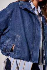 Campera bomber de jean con corte oversize, cierre frontal y cuello alto con botones a presión. Presenta mangas amplias y puños ajustados.
