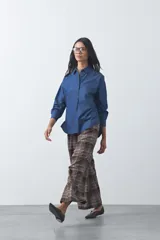 Camisa de jean en tencel con silueta amplia, hombros caídos, cuello clásico y cierre frontal con botones. Presenta ruedo curvo con tajos laterales y pliegue en la espalda.
