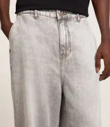 Pantalón de jean corte baggy, de tiro alto y pierna ancha, con diseño de cinco bolsillos, trabillas para cinturón y cierre frontal con botón y cremallera.