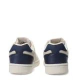 Championes urbanos Umbro modelo Milo, con diseño de paneles en tonos beige y blanco, y detalles en azul marino en el talón y logo lateral. Presenta puntera perforada y suela de goma al tono.