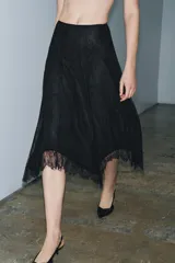 Falda midi negra de tiro medio, confeccionada en tejido de encaje con forro interior a tono. Presenta un bajo asimétrico con terminación en línea evasé y cierre lateral oculto.