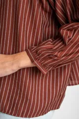 Blusa de manga larga con diseño a rayas verticales, cuello redondo con pequeña abertura frontal abotonada y mangas con puños elásticos.