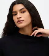 Blusa de punto de corte holgado, color negro, con cuello redondo elevado y mangas cortas amplias con sisa desplazada.