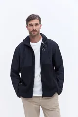 Campera con capucha de diseño híbrido, combinando paneles de tejido polar suave y secciones de tela técnica resistente al viento. Presenta cierre frontal completo, bolsillos laterales y un bolsillo con cierre en el pecho.