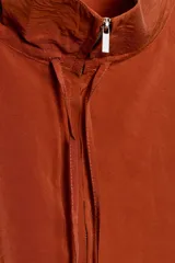 Chaqueta color naranja óxido de tejido fluido, con cuello subido, manga larga acabada en elástico, bolsillos laterales de vivo, bajo elástico y cierre frontal con cremallera.