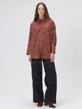 Camisa de seda con cuello camisero, manga larga y bolsillo frontal. Presenta un diseño estampado geométrico de cuadrados en tonos marrones y azul oscuro.