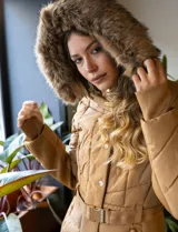 Campera acolchada color camel, con costuras diagonales y capucha forrada con piel sintética marrón. Posee cierre frontal oculto, botones a presión y cinto ajustable con hebilla metálica dorada con logo.