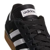 Championes Adidas Busenitz Pro, modelo de skate en color negro con las icónicas tres tiras blancas laterales y suela de goma color caramelo. Presenta una lengüeta larga característica y detalles en dorado.