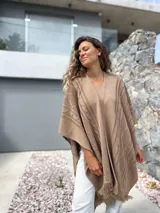 Ruana tejida en color beige, con diseño de trenzas verticales y terminación de flecos en el ruedo. Presenta una caída holgada y abierta al frente.