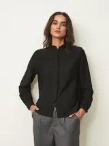 Camisa de manga larga en color blanco, con cuello mao y detalle de volados sutiles en el borde. Presenta cierre frontal oculto con botones y puños con volados.