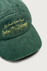 Gorra de siete paneles verde oscuro con efecto lavado, visera curva y bordado frontal en tono amarillo con la inscripción 'Bahia Montego'. Cuenta con ajuste posterior.
