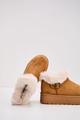 Bota corta tipo moon boot color camel, con plataforma plana y detalle de piel sintética en el borde superior. Incluye una tira decorativa con hebilla metálica en el lateral.