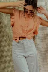 Blusa color salmón sin mangas, con volados en los hombros, cuello alto con ribete fruncido y cierre frontal con botones.