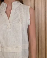 Musculosa marrón sin mangas, con cuello alto, escote en V y detalles de pespuntes blancos en contraste. Presenta pliegues y alforzas frontales.