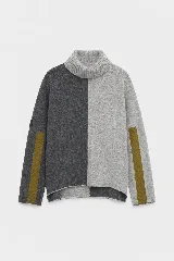 Polera de tejido lambswool con diseño bicolor en gris oscuro y gris claro. Presenta cuello alto, corte holgado y mangas largas con franjas verticales en color mostaza.