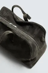 Bolso de viaje de gran tamaño confeccionado en piel con acabado de serraje. Cuenta con un compartimento principal con cierre de cremallera e imanes, interior con bolsillo con cierre y bolsillo plano, y dos asas de mano de piel.