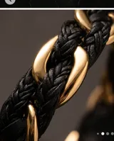 Pulsera de diseño trenzado que combina tiras de cuero negro con eslabones de acero en tono dorado. Cuenta con un cierre magnético integrado.