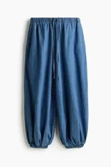 Pantalón tobillero de corte holgado en denim de algodón rígido, con cintura elástica con cordón de ajuste, bolsillos laterales discretos y piernas globo con elástico en los tobillos.
