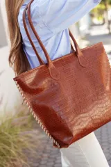 Bolso tipo tote de cuero color marrón con textura tipo cocodrilo, doble asa de hombro y cierre superior con cremallera.