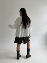 Blusa blanca de corte holgado con cuello mao, botones frontales y detalles bordados en el pecho. Presenta mangas largas con puños con volados.