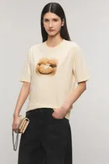 Remera oversize de jersey de algodón color beige claro, con cuello redondo, mangas cortas y estampa frontal de unos labios con un caramelo.