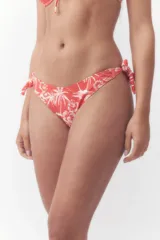 Bombacha de bikini color naranja con estampado tropical de palmeras y flores blancas, con tiras laterales para atar con lazo.