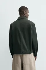 Cazadora relaxed fit color verde oscuro, confeccionada en tejido de algodón. Cuenta con cuello solapa, manga larga con puño abotonado, bolsillos plastrón con solapa en la cadera y cierre frontal de botonadura.