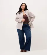 Camisa plus size alargada de Ashua, confeccionada en tela anarruga con diseño a rayas en tonos marrón y blanco. Presenta cuello inglés, cierre frontal con botones y mangas largas.