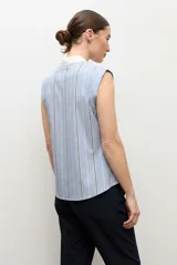 Camisa sin mangas celeste con rayas verticales blancas y finas líneas oscuras, con cuello camisero blanco y cierre frontal de botones.