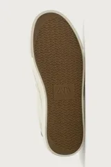 Zapatilla casual de tejido de algodón color beige con detalles en verde y un parche negro en el talón. Cuenta con suela de goma texturizada a contraste.