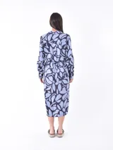 Vestido camisero midi de manga larga, con cuello y botones frontales, ajustado a la cintura con un lazo. Presenta un estampado abstracto en tonos azul claro y azul oscuro/negro.