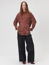 Camisa de seda con estampado geométrico de cuadrados en tonos rojizos y marrones. Presenta cuello camisero, cierre frontal con botones, bolsillo en el pecho y mangas largas con puños abotonados.