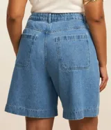 Bermuda de jeans de algodón, color azul medio, de corte amplio y largo hasta la rodilla. Presenta tiro alto con ajuste elástico interno en la cintura y bolsillos frontales.