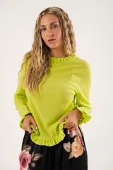 Blusa verde lima con textura arrugada, cuello redondo con volantes y mangas largas con puños elásticos.