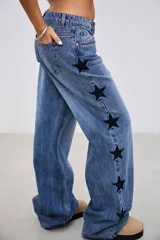 Pantalón de jean tiro medio-bajo, de corte holgado y pierna ancha, con diseño de estrellas oscuras aplicadas a lo largo de la pierna.
