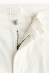 Jean tobillero de corte slim straight y tiro alto, en denim de algodón blanco con ligero stretch, cinco bolsillos, cierre de botón y cremallera, y pliegues marcados al frente y en la espalda.