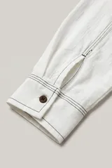 Camisa de manga larga color blanco, con cuello clásico, cierre frontal con botones marrones y costuras pespunteadas en contraste.