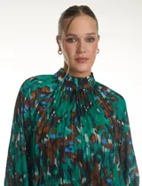Blusa de gasa plisada con estampado abstracto en tonos verdes, azules y marrones. Presenta cuello alto, mangas largas abullonadas con puños abotonados y un corte holgado con caída fluida.