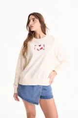 Buzo blanco sin frisa, de manga larga, con corte holgado y pequeños bordados coloridos en el pecho.