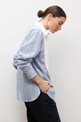 Camisa de manga larga celeste a rayas con pechera blanca lisa en el frente, cuello camisero y botones frontales.