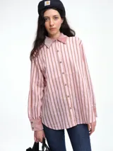 Camisa de corte relajado con estampado de rayas verticales en tonos rosado y marrón. Presenta cuello clásico, puños y detalles en terciopelo rosado, con cierre frontal de botones.