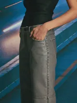 Pantalón de corte recto y tiro medio, confeccionado en material con acabado encerado color gris oscuro. Presenta costuras decorativas verticales a lo largo de las piernas y costura horizontal a la altura de la rodilla, con bolsillos laterales y cierre frontal.