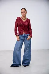 Blusa de manga larga color bordó, con tejido de punto calado, escote en V con volados y cierre frontal anudado.