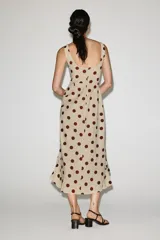 Vestido midi de mezcla de lino y viscosa en color beige con estampado de lunares bordó. Cuenta con escote recto, tirantes anchos y un volante lateral en cascada que recorre el frente hasta el bajo asimétrico.