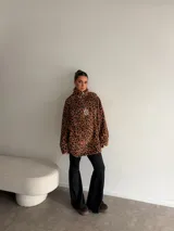 Buzo de peluche con estampado animal print, cuello alto con cierre frontal parcial y detalle de etiqueta decorativa en el pecho.