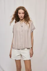 Camisa de manga corta color celeste, confeccionada en viscosa fluida, con silueta amplia y escote redondo con frunces y lazo para anudar.