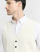 Chaleco de vestir color crudo, con cuello en V y cierre frontal con botones. Posee dos bolsillos ribeteados en la parte inferior y uno tipo ojal en el pecho.